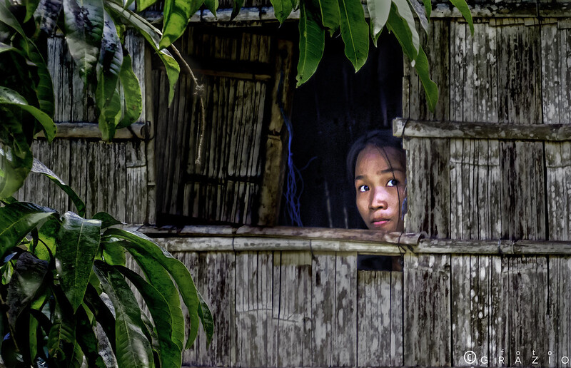 woman in a rough hut peeking out of a window