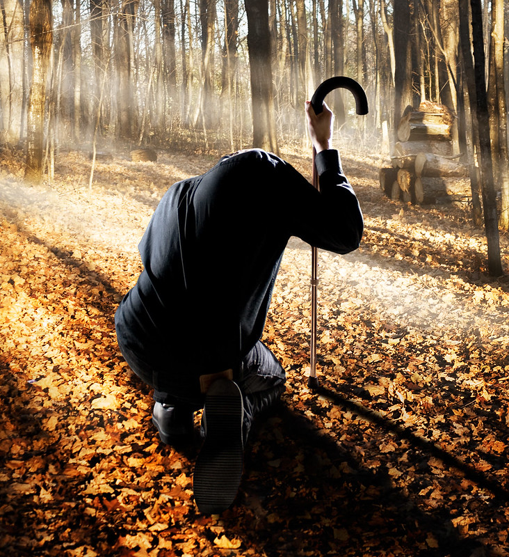 man with a cane standing bent over in a forest