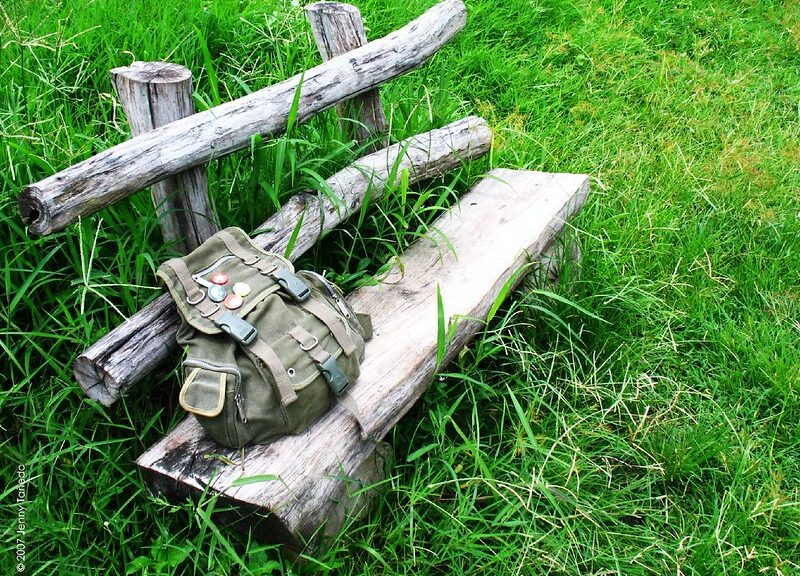 old rustic park bench in tall grass with backpack set on it