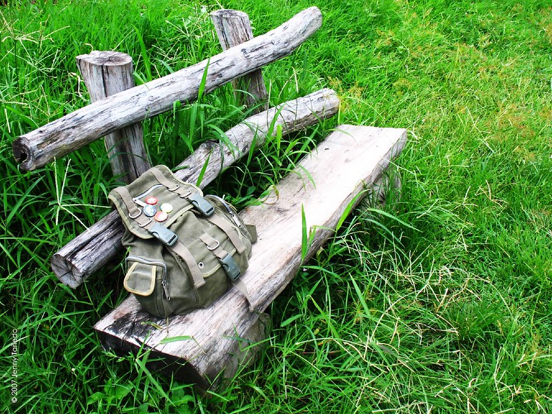 old rustic park bench in tall grass with backpack set on it