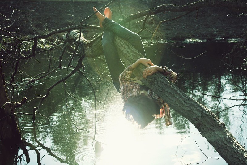 girl clinging to a branch hanging over a river, metaphor for being willing to try