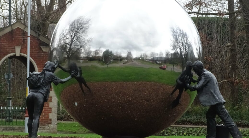 sculpture of two human figures (male and female) pushing on a shiny reflective metal sphere