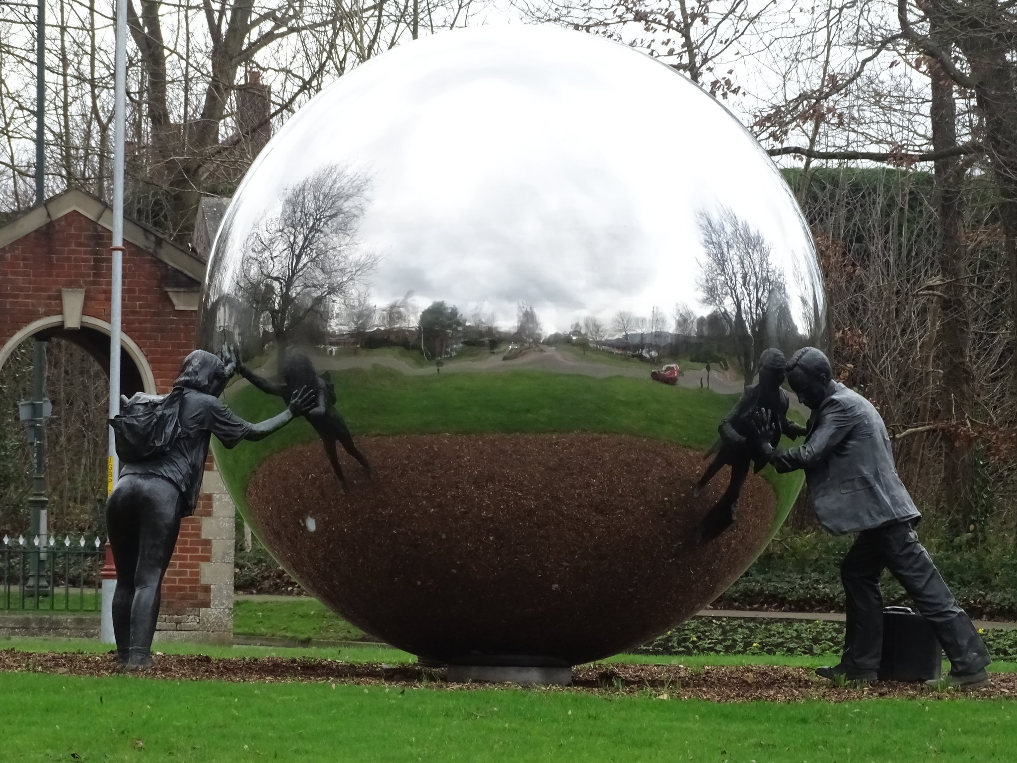 sculpture of two human figures (male and female) pushing on a shiny reflective metal sphere