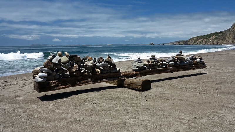 large collection of balanced stacks of rocks on a driftwood teeter-totter