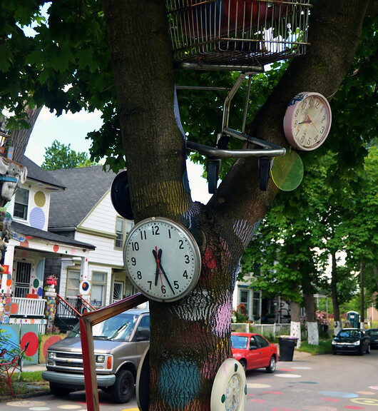 tree in foreground decorated with painted dots and clocks in neighborhood with similarly decorated houses