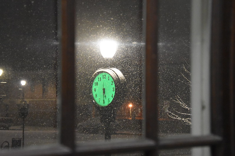 lighted clock on a post glowing green outside a window