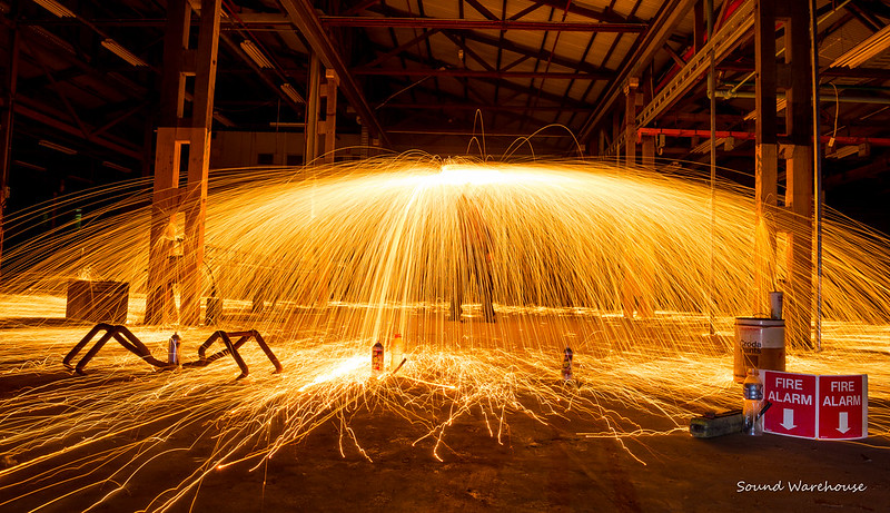 in a warehouse, there's an arching umbrella of sparks with someone under it
