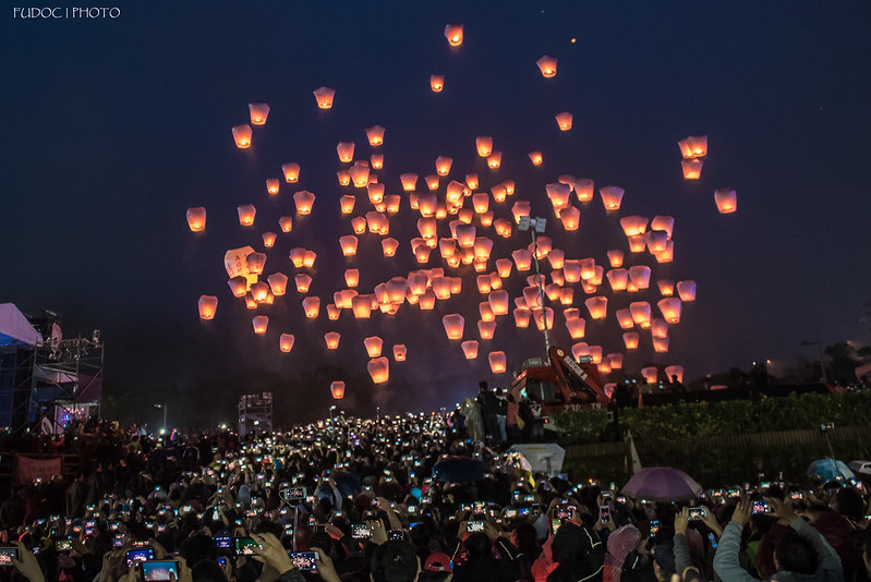 lighted paper lanterns floating above a crowd in the night sky
