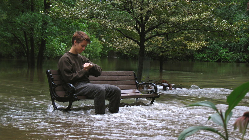 young man sitting on a park bench in the middle of a river, checking his watch